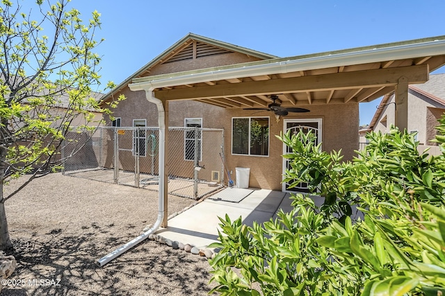 rear view of house featuring stucco siding, a gate, ceiling fan, and fence