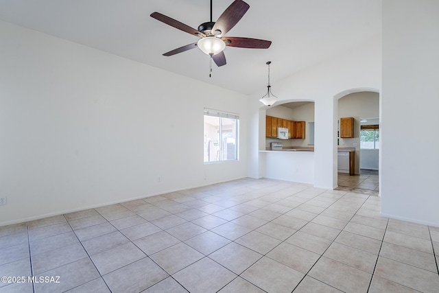 unfurnished living room with light tile patterned flooring, ceiling fan, arched walkways, high vaulted ceiling, and baseboards