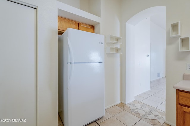 kitchen featuring light countertops, arched walkways, freestanding refrigerator, light tile patterned floors, and visible vents