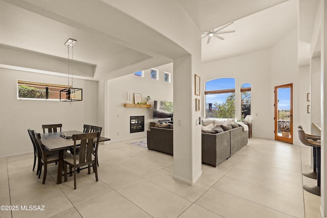 dining area with light tile patterned floors, plenty of natural light, ceiling fan with notable chandelier, and a glass covered fireplace