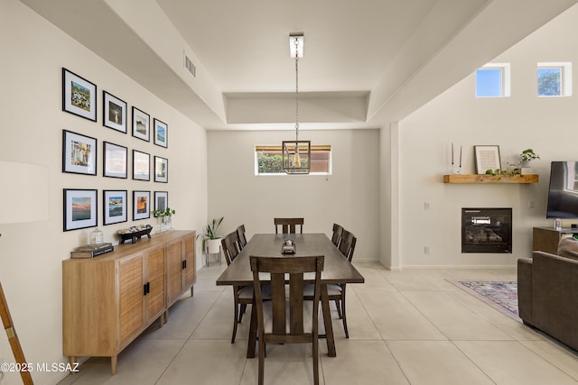 dining room with visible vents, a raised ceiling, a glass covered fireplace, and light tile patterned floors