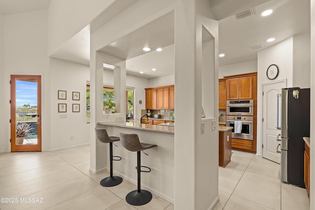 kitchen featuring brown cabinets, light stone counters, stainless steel appliances, light tile patterned floors, and visible vents