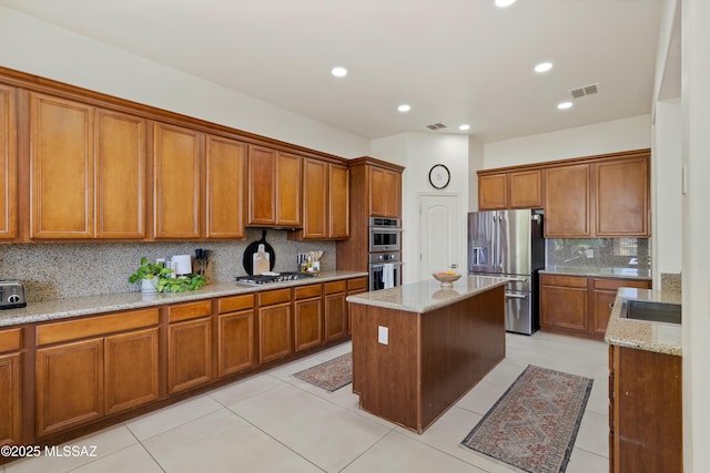 kitchen with decorative backsplash, brown cabinetry, visible vents, appliances with stainless steel finishes, and a center island