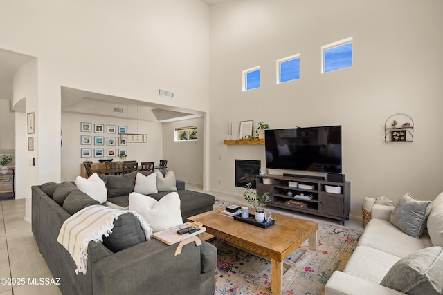 living room with a high ceiling, visible vents, a glass covered fireplace, and light tile patterned floors
