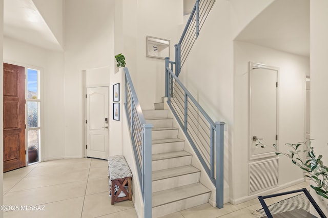 stairs featuring tile patterned flooring, a high ceiling, baseboards, and visible vents