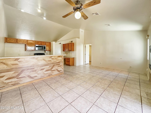 10084 E Bryonwood Ln, Tucson, AZ 85730 - kitchen with stainless steel microwave, light tile patterned floors, light countertops, brown cabinetry, and lofted ceiling
