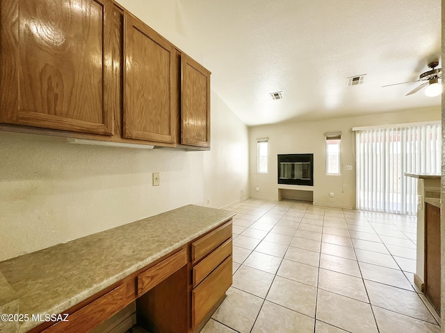 10084 E Bryonwood Ln, Tucson, AZ 85730 - kitchen featuring a glass covered fireplace, ceiling fan, brown cabinetry, open floor plan, and light tile patterned flooring
