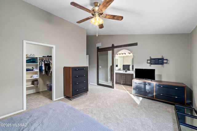 bedroom with light colored carpet, a barn door, a spacious closet, lofted ceiling, and ensuite bath