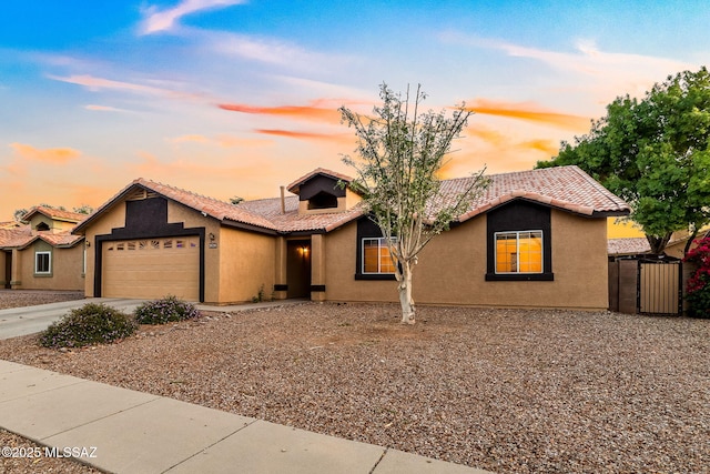 view of front facade featuring an attached garage, stucco siding, a gate, a tiled roof, and driveway
