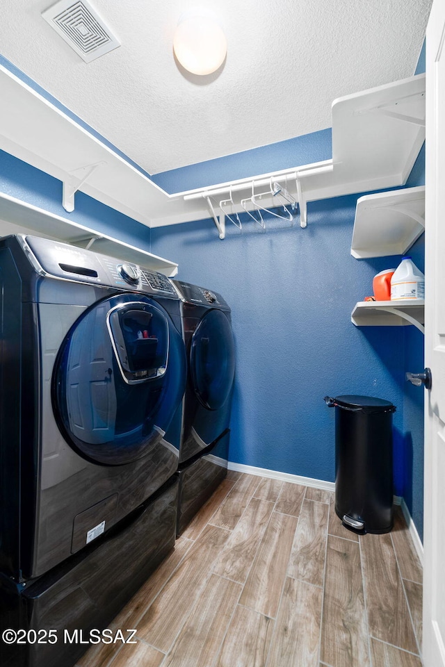 clothes washing area with laundry area, visible vents, wood finished floors, washer and dryer, and baseboards