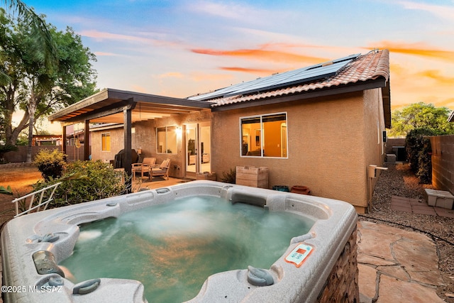 back of property at dusk with a hot tub, stucco siding, a fenced backyard, solar panels, and a patio area