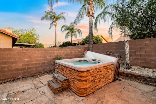 patio terrace at dusk with a hot tub and a fenced backyard