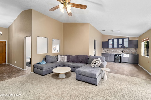living room with light carpet, beverage cooler, baseboards, high vaulted ceiling, and a ceiling fan
