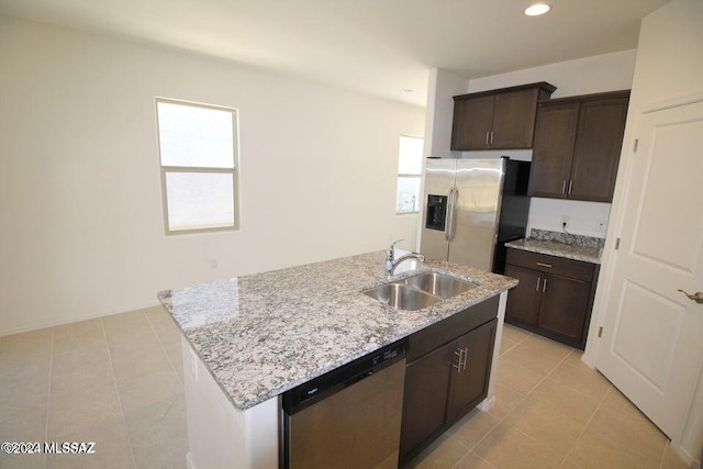 kitchen with dark brown cabinetry, light stone countertops, a sink, appliances with stainless steel finishes, and light tile patterned floors