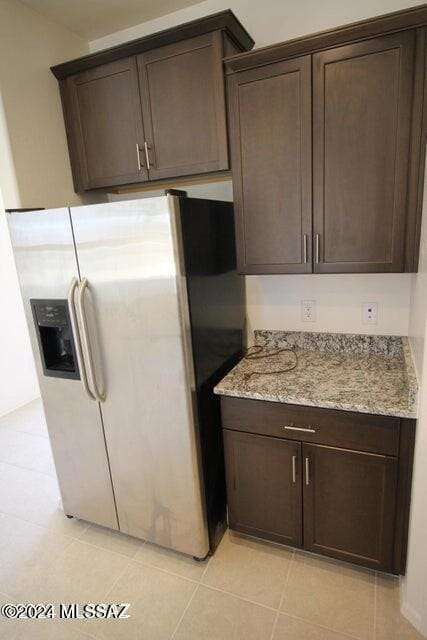 kitchen with dark brown cabinets, light stone counters, and fridge with ice dispenser
