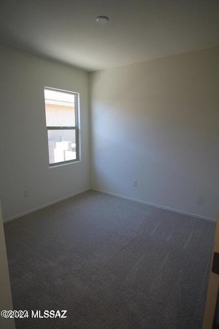 spare room featuring dark colored carpet and baseboards
