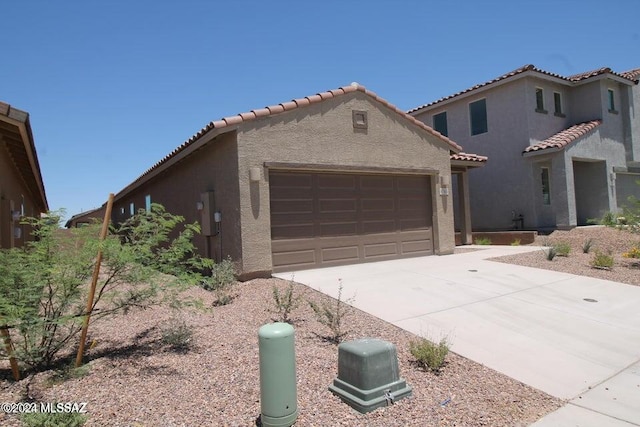 mediterranean / spanish house featuring a garage, stucco siding, driveway, and a tile roof