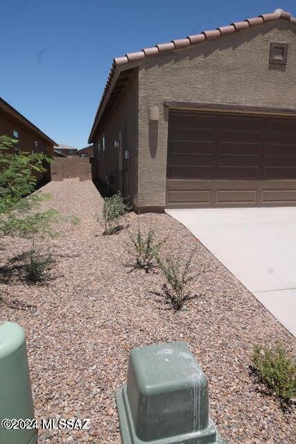 view of side of property featuring fence, a garage, driveway, and stucco siding