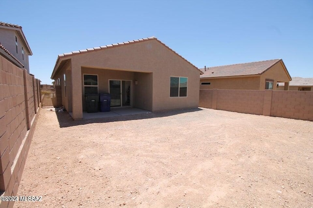 rear view of property featuring a tile roof, a fenced backyard, a patio area, and stucco siding