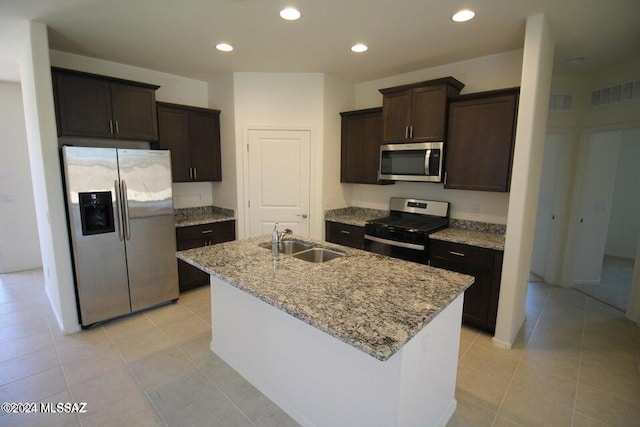 kitchen with dark brown cabinetry, light stone counters, a sink, an island with sink, and stainless steel appliances