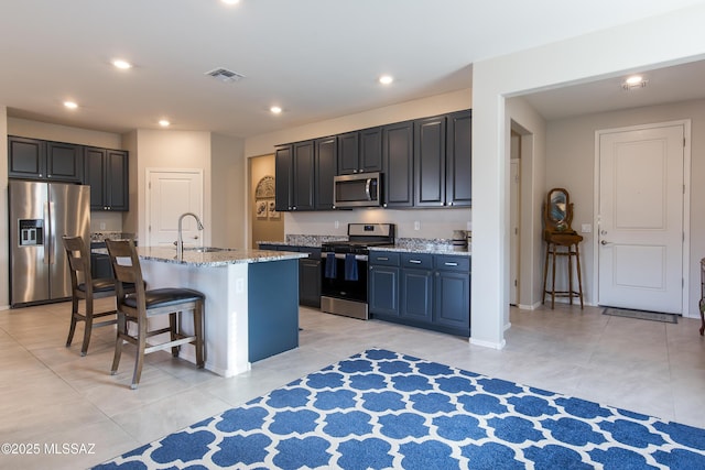 kitchen with light stone countertops, a breakfast bar, a sink, stainless steel appliances, and light tile patterned floors