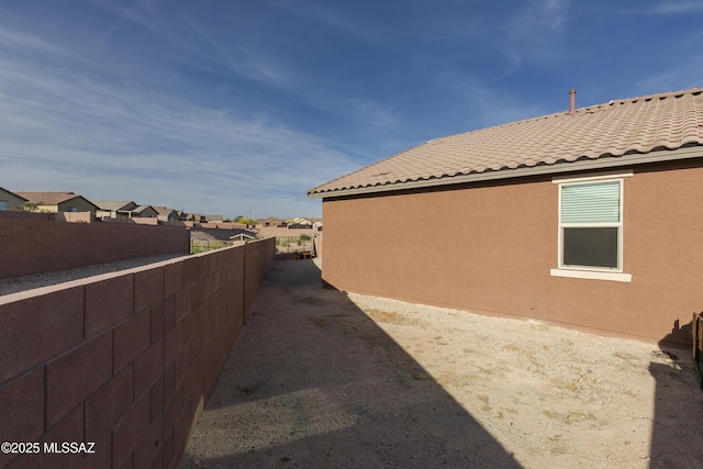 view of property exterior featuring fence, a tiled roof, stucco siding, and a residential view
