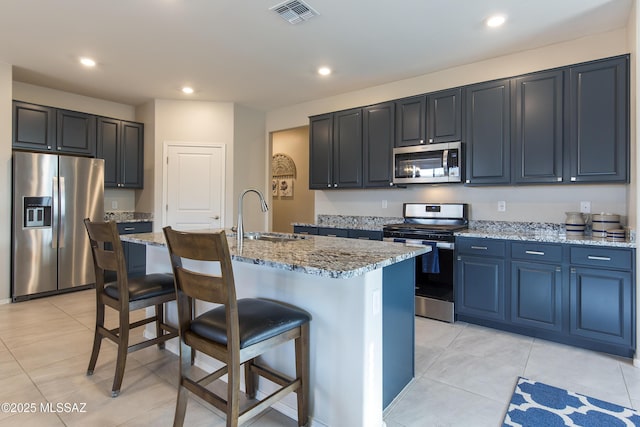 kitchen featuring visible vents, a breakfast bar, light stone counters, a sink, and appliances with stainless steel finishes
