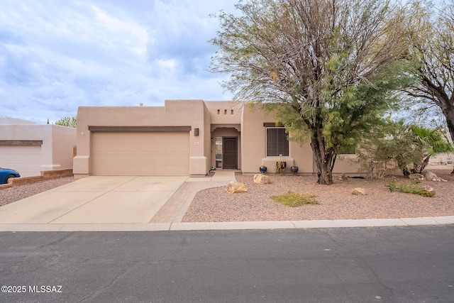 pueblo-style house with an attached garage, driveway, and stucco siding