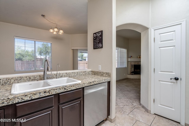 kitchen with dark brown cabinets, a sink, a fireplace, light countertops, and dishwasher