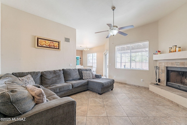 living room featuring visible vents, light tile patterned flooring, baseboards, a tiled fireplace, and a ceiling fan