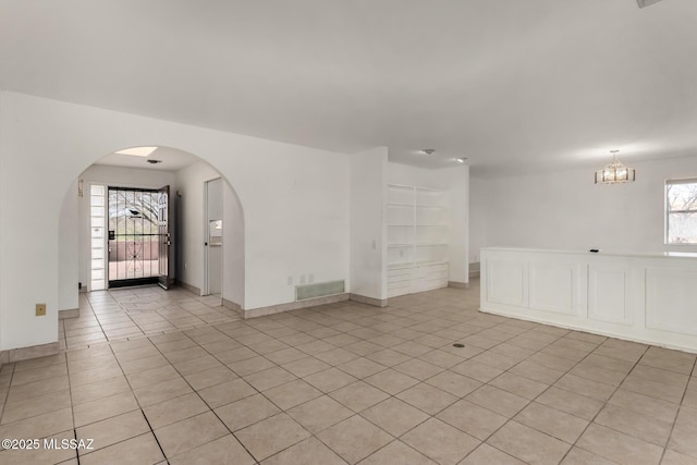 unfurnished room with arched walkways, a chandelier, baseboards, light tile patterned floors, and visible vents