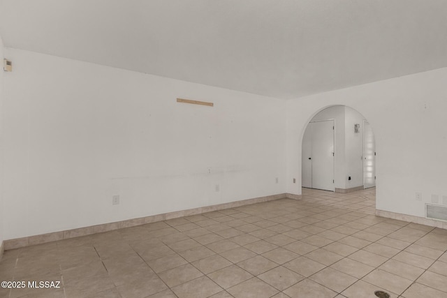 spare room featuring light tile patterned floors, arched walkways, baseboards, and visible vents