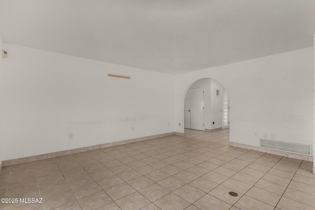 empty room with arched walkways, baseboards, visible vents, and light tile patterned floors