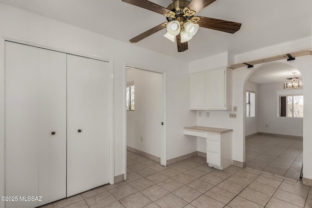kitchen with arched walkways, light tile patterned floors, light countertops, ceiling fan with notable chandelier, and white cabinetry