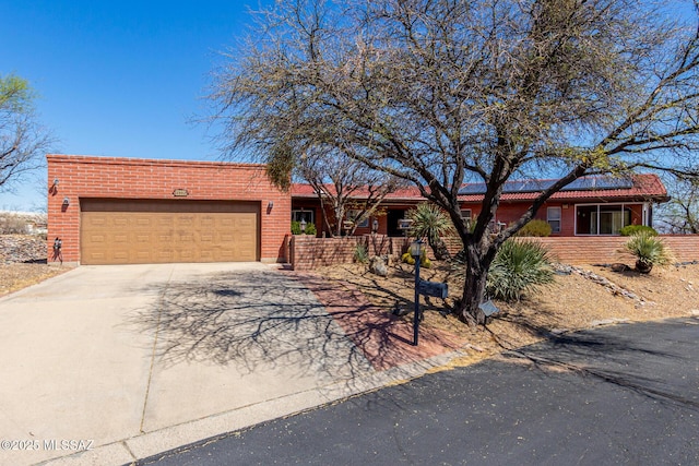 ranch-style house with brick siding, a garage, driveway, and solar panels
