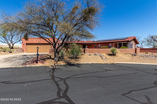ranch-style house featuring brick siding, an attached garage, driveway, and solar panels