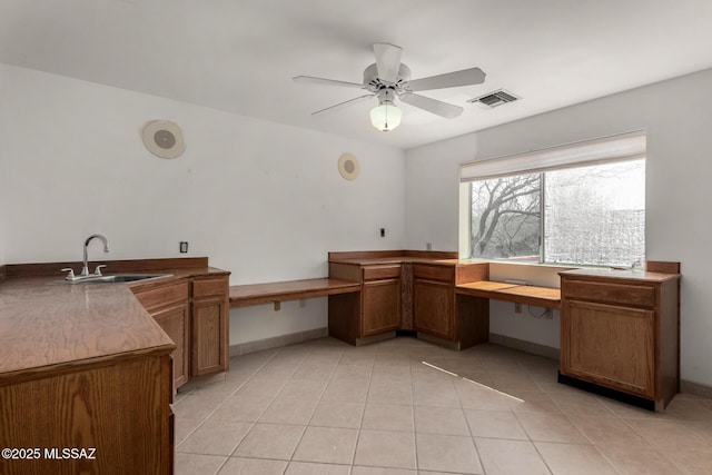 unfurnished office with ceiling fan, visible vents, built in desk, a sink, and light tile patterned flooring