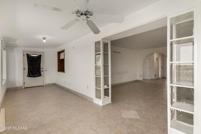spare room with arched walkways, ceiling fan, light tile patterned floors, and baseboards