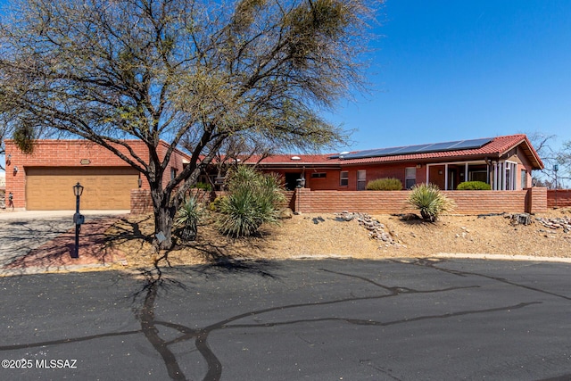 single story home featuring driveway, a garage, brick siding, fence, and roof mounted solar panels