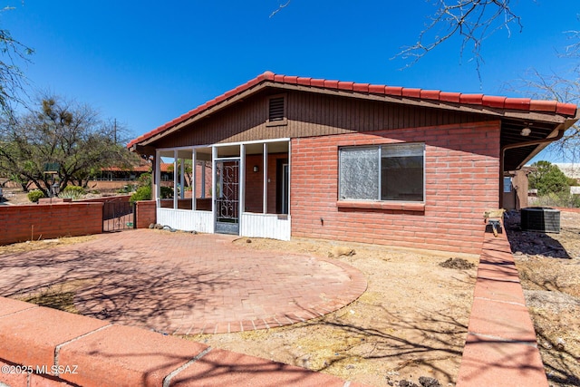 rear view of property featuring central AC, brick siding, a sunroom, a patio area, and a tiled roof