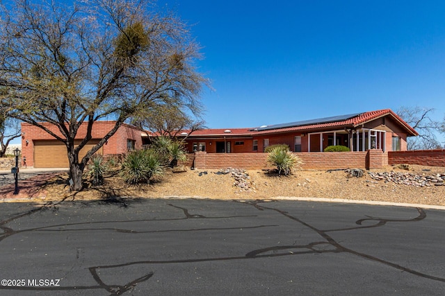 ranch-style home featuring an attached garage, concrete driveway, solar panels, and brick siding