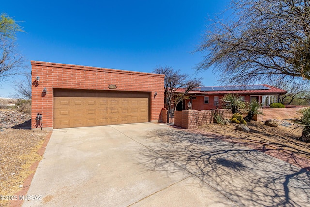 view of front of house with fence, brick siding, roof mounted solar panels, an attached garage, and driveway