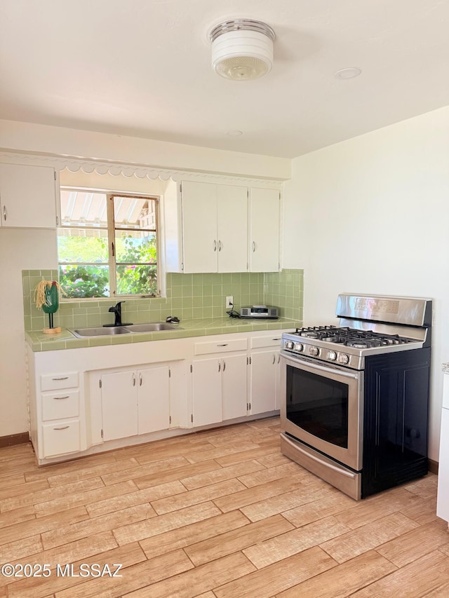 kitchen featuring stainless steel range with gas stovetop, a sink, white cabinets, and tile counters