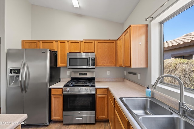 kitchen with appliances with stainless steel finishes, a sink, light wood-style floors, light countertops, and lofted ceiling
