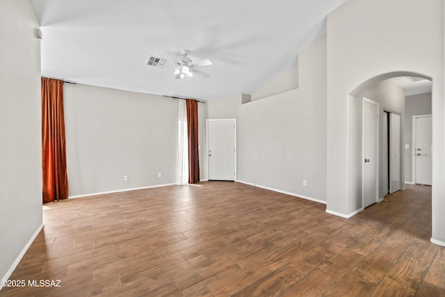 unfurnished room with arched walkways, a ceiling fan, baseboards, wood finished floors, and visible vents