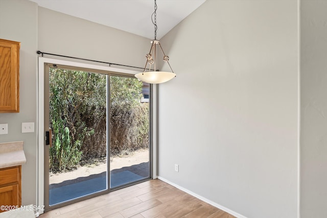 unfurnished dining area featuring baseboards, light wood finished floors, and lofted ceiling