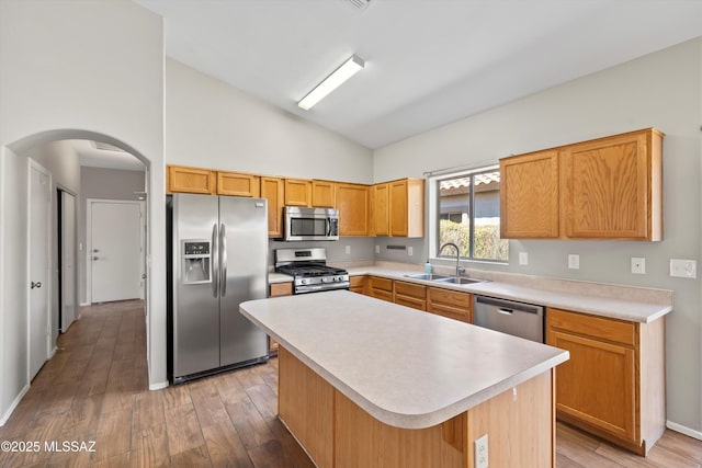 kitchen with appliances with stainless steel finishes, a sink, light countertops, arched walkways, and light wood-style flooring