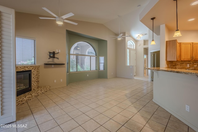 unfurnished living room featuring ceiling fan, vaulted ceiling, light tile patterned floors, and a tile fireplace