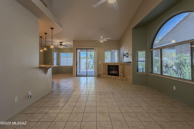 unfurnished living room with a ceiling fan, a fireplace, light tile patterned floors, baseboards, and high vaulted ceiling