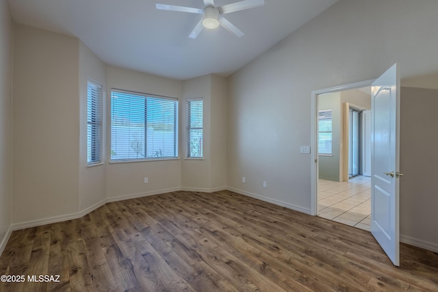unfurnished room with baseboards, a ceiling fan, wood finished floors, and vaulted ceiling
